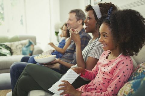 Младо многоетническо семейство гледа филми и яде пуканки на дивана