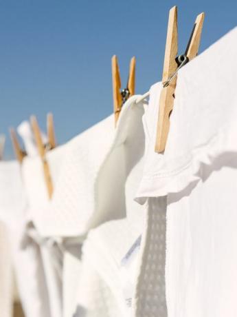 бели дрехи, закачени да изсъхнат на пералня на светлия топъл слънчев фон, е ясно синьо небе