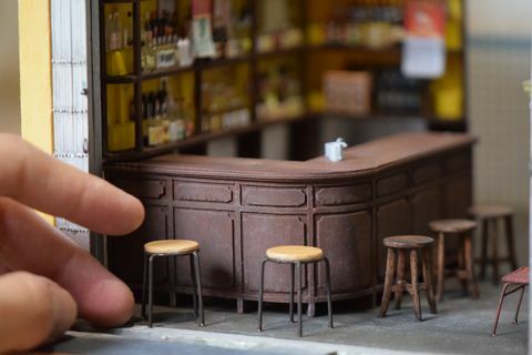 едър план на миниатюрна реплика на бар, с бар столове и човешка ръка за кантар