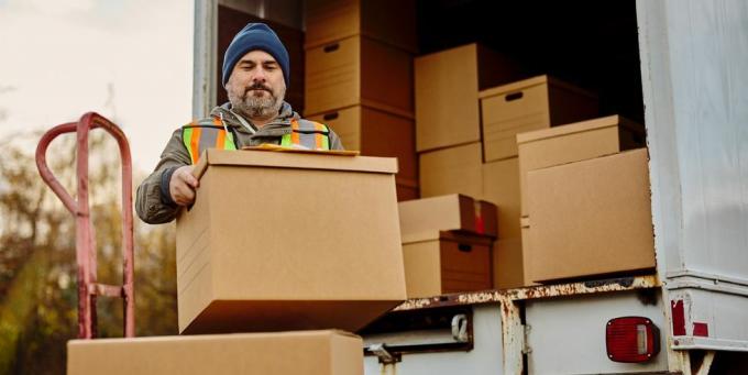 мъжки работник разтоварва картонени кутии от микробус за доставка