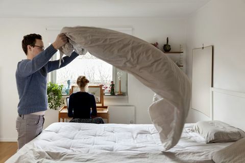 Човек прави легло, докато жена работи на маса в спалнята
