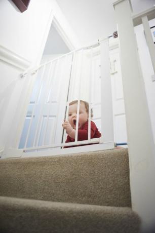 Безопасна порта за бебета на стълби: Момченце на площадката на дома си. Той е зад предпазна порта на бебето, която го спира от опасността от стълбището.