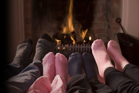 Крака (сиви, тъмносини и розови чорапи) пред печка на дърва