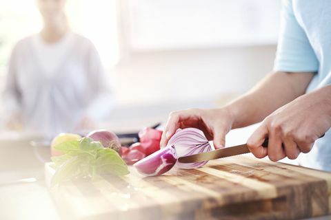 Жена нарязва червен лук върху дъска за рязане в кухнята